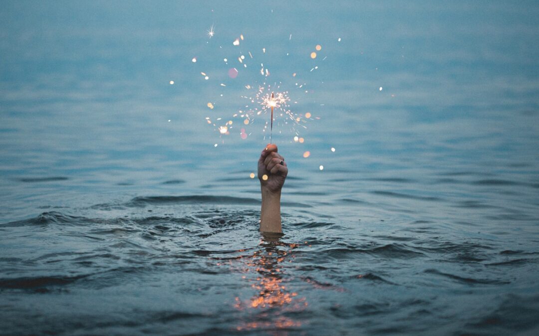 Image of a person's hand holding up a sparkler from the sea