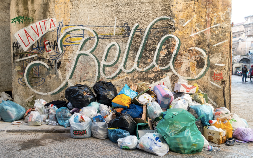 Image of a wall that says "La Vita Bella" surrounded by trash bags