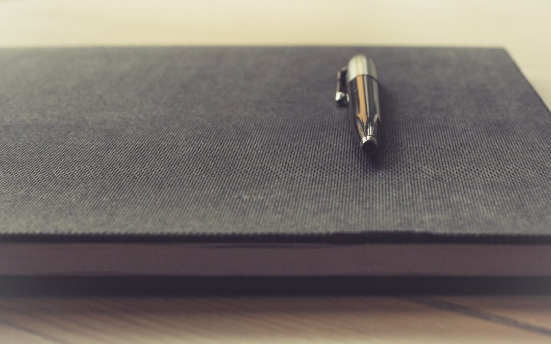 Photo of a pen resting on a journal by Thomas Martinsen via Unsplash
